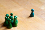 A group of green plastic pawn figures facing a solitary green plastic pawn figure