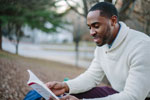 A Black man in a cozy sweater reading outdoors
