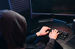 Person in a black hoodie typing on a dark computer
