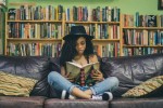 Teen girl reading on a couch in a library.