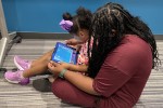 Woman with a young girl in her lap, both watching a tablet computer