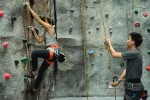 Woman on a rock climbing wall with a man holding her support line