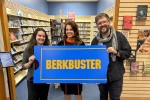 Berkley (Michigan) Public Library holding up Berkbuster sign in front of the library's video store-themed media section