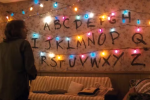 Screencap from Stranger Things showing a wall of Christmas lights and letters