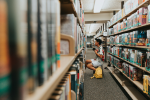 Boy examining books on llbrary shelves