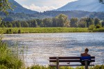 Person sitting on a bench in front of a peaceful mountain lake